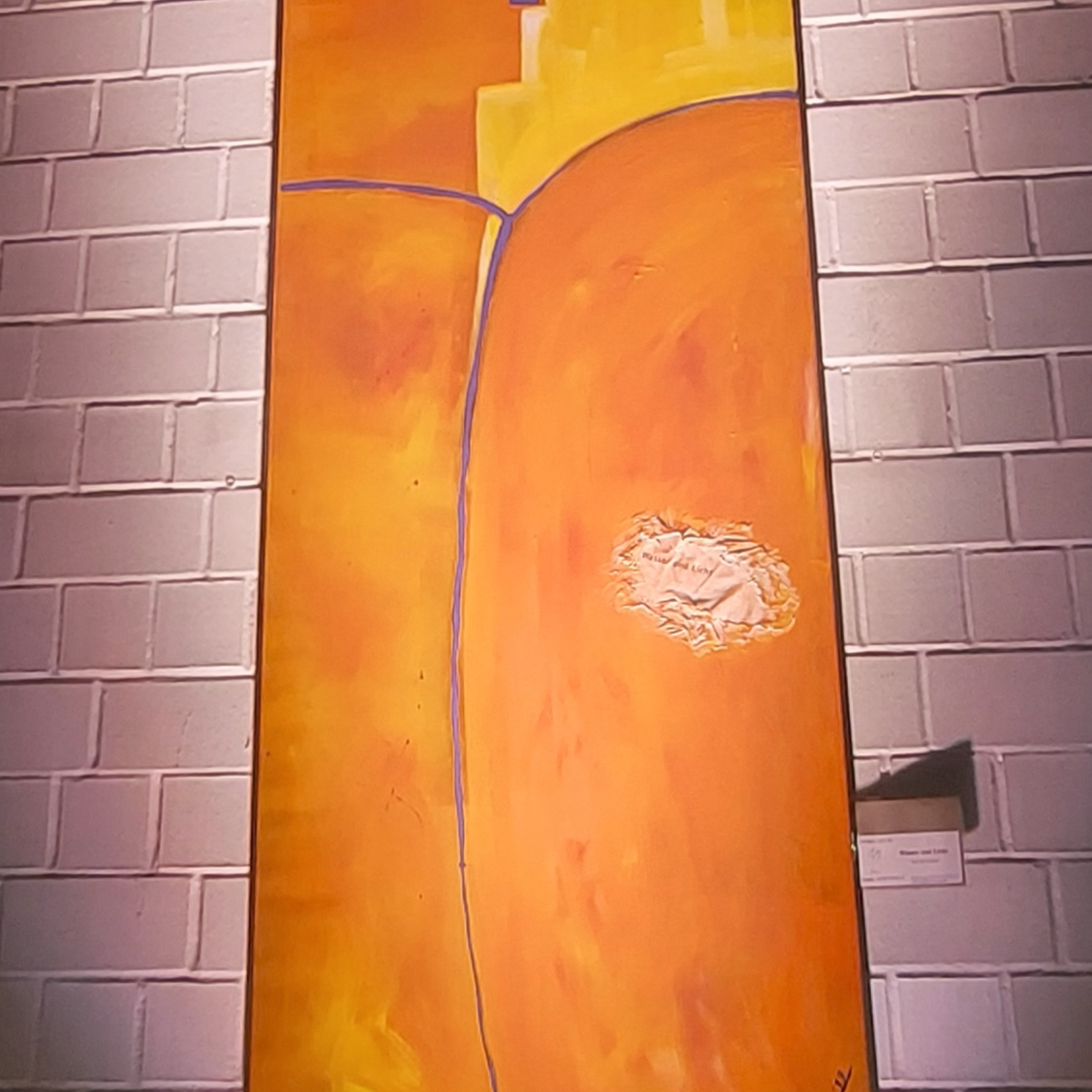 großformatige Malerei in Orange, auf einer weißen Backsteinwand, blaue Linien als Tau-Kreuz