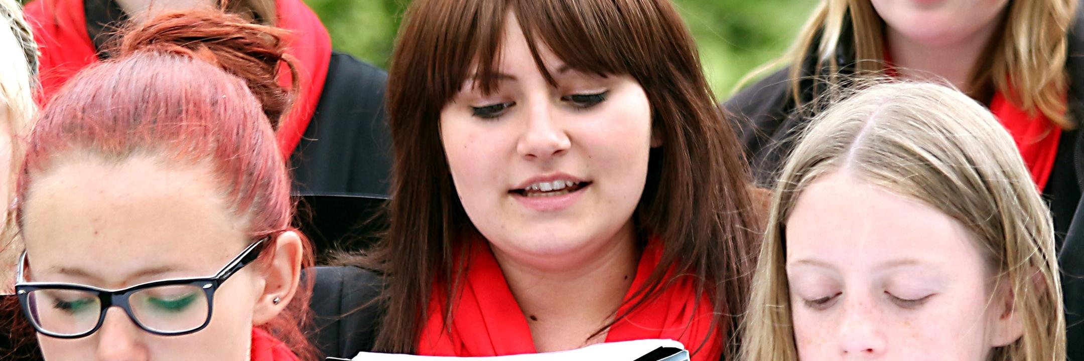 Junge Frauen singen mit Begeisterung aus schwarzen Liedmappen.