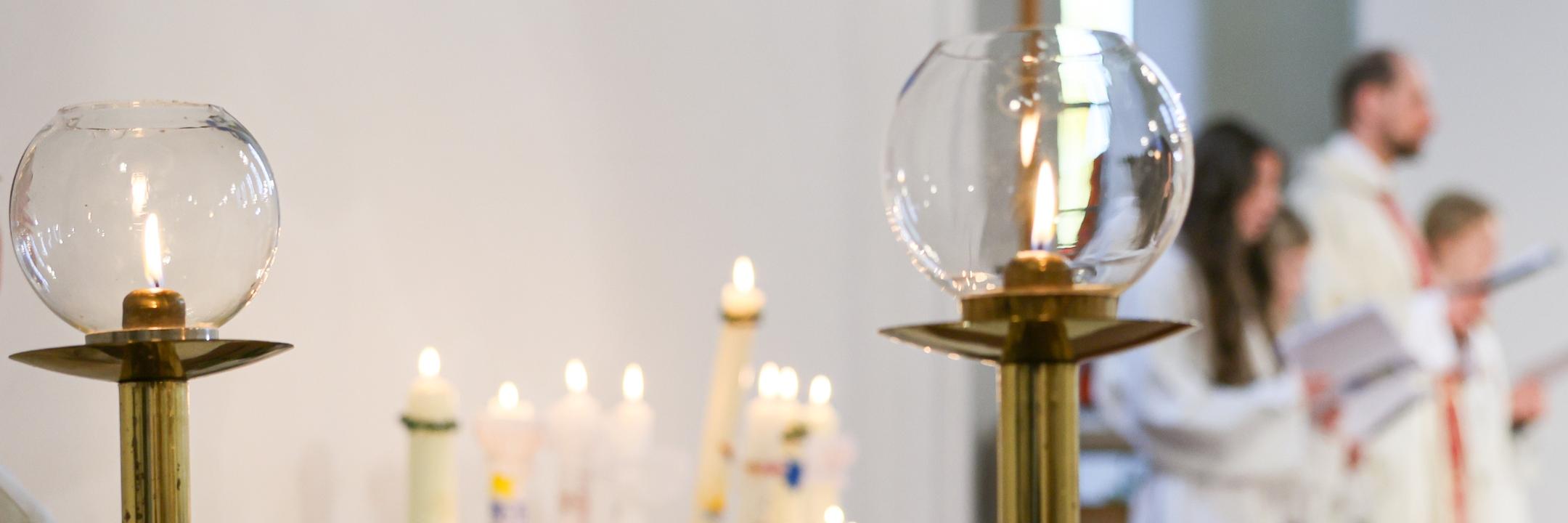 Altar mit 2 Leuchter im Vordergrund, in der Mitte Kommunionkerzen, im Hintergrund Priester und Messdienerinnen