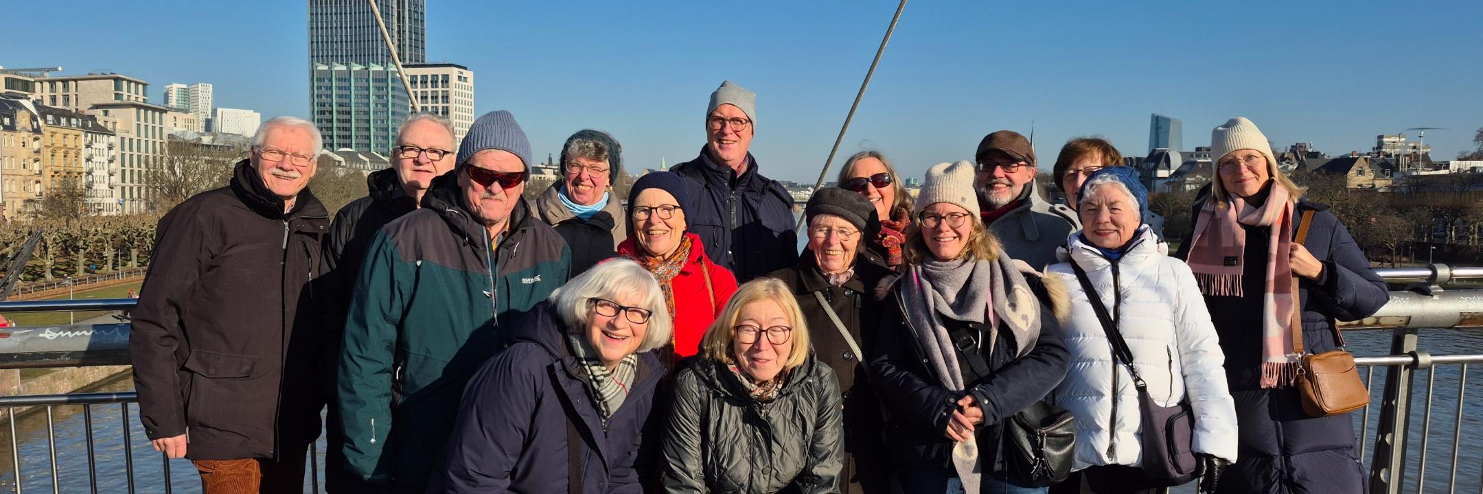 Eine Gruppe fröhlicher Leute steht bei strahlendem Winterwetter auf einer Brücke über dem Main auf dem Weg zum Städel-Museum