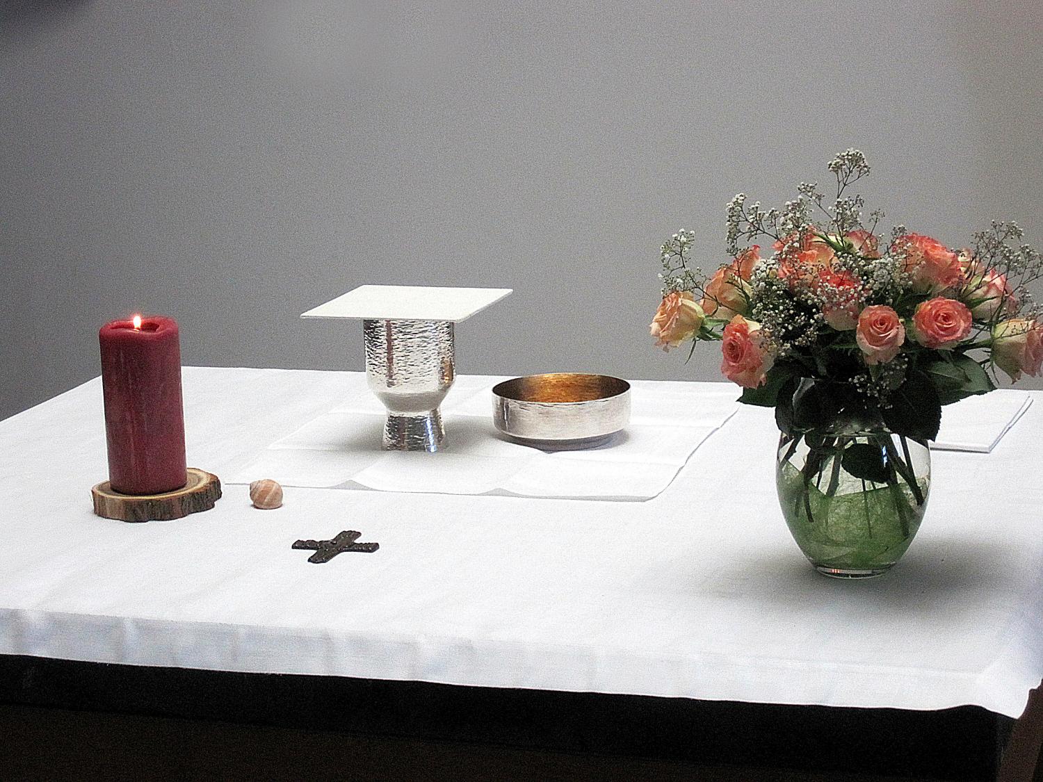 Altar mit brennender Kerze, Kelch, Hostienschale, Kreuz und einem Strauß Rosen.