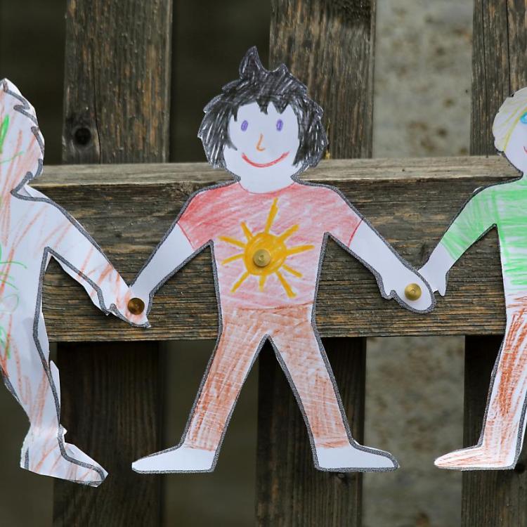 Drei gebastelte Figuren aus Papier sind auf einen Zaun geklebt.