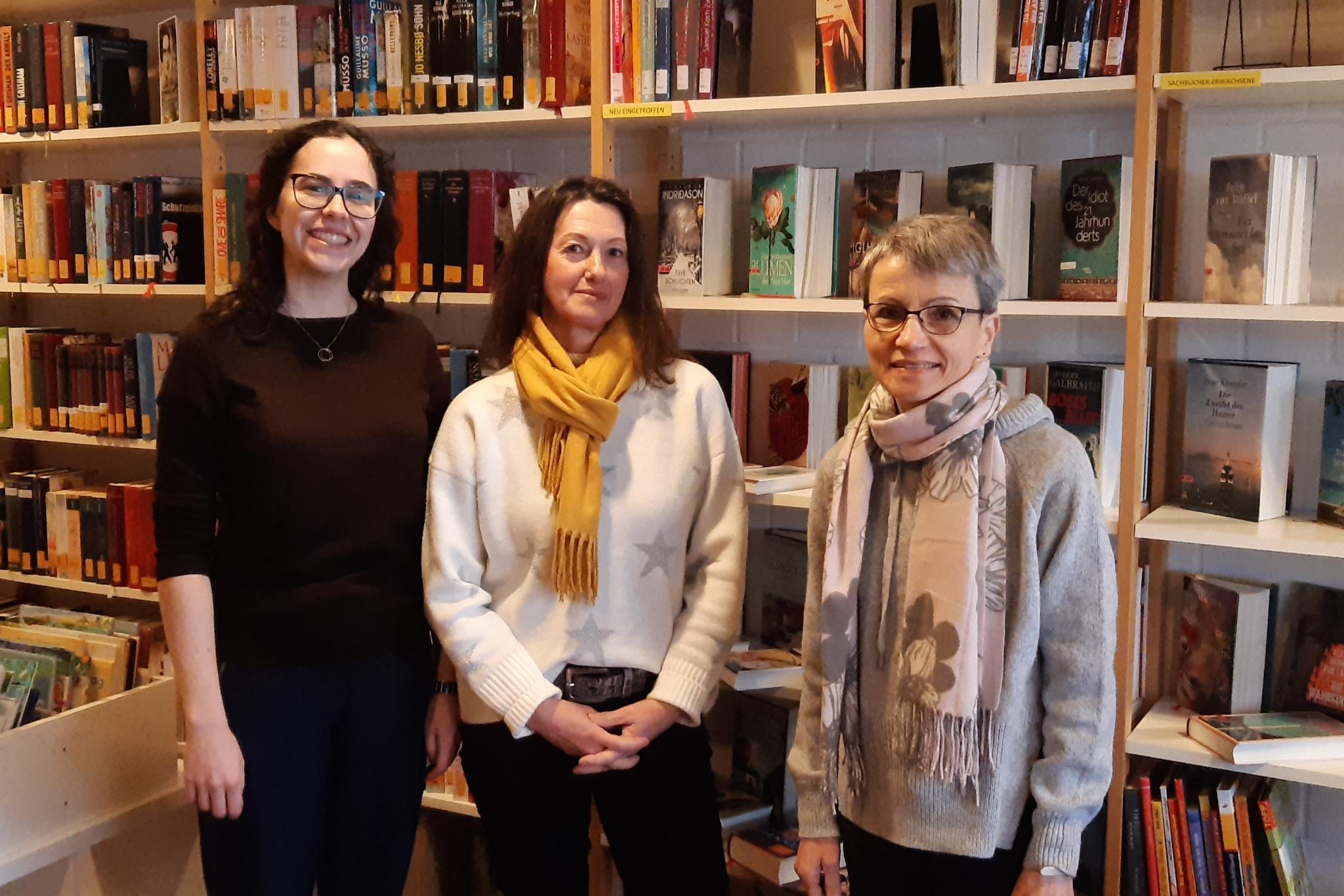 Die drei Bücherei-Betreuerinnen in der Bücherei vor Regalen.