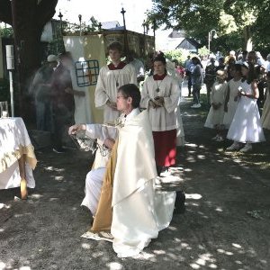 Altar in einem Park, davor ein Priester kniend, Messdiener und weitere Menschen.
