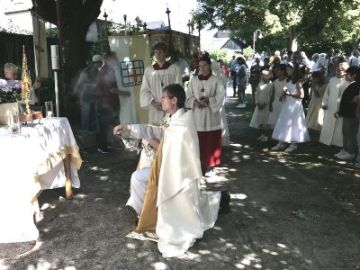 Altar in einem Park, davor ein Priester kniend, Messdiener und weitere Menschen.