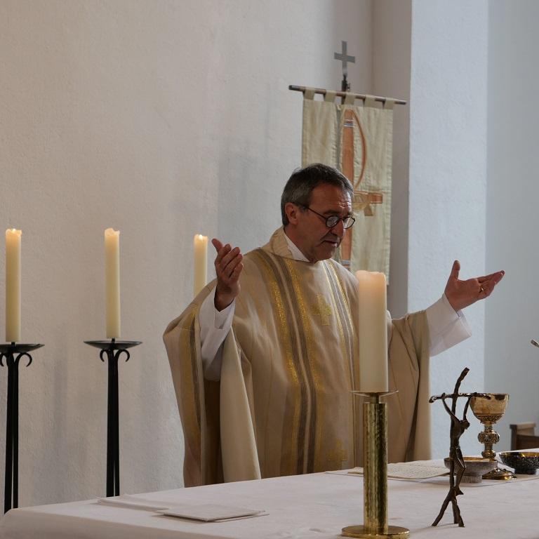 Ein Priester in weißem Messgewand an einem Altar mit ausgebreiteten Händen.