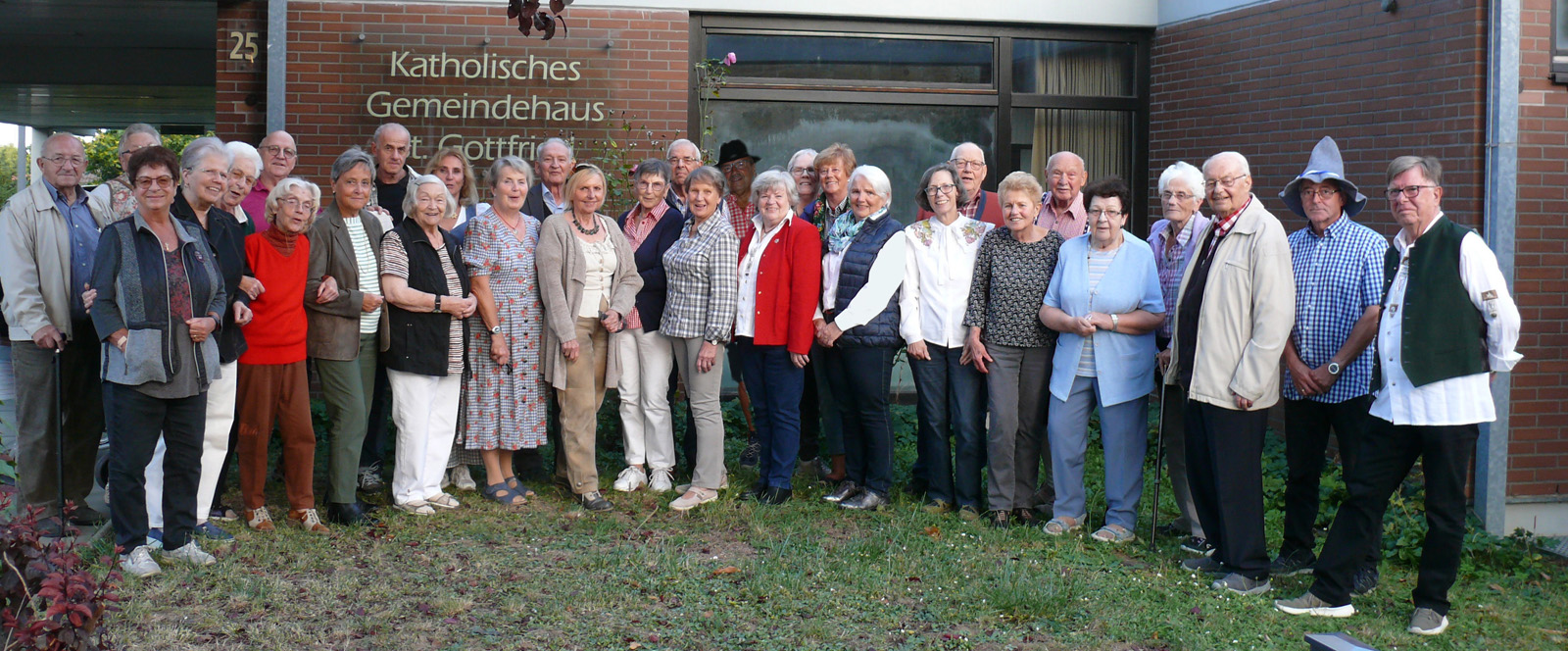 Rund 25 Mitglieder der Gruppe 50+ stehen im Halbkreis und lächeln in die Kamera.