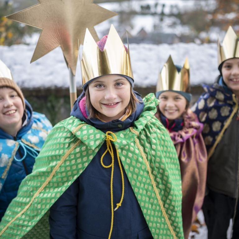 Vier Kinder, gekleidet als Sternsinger, laufen durch die Straße