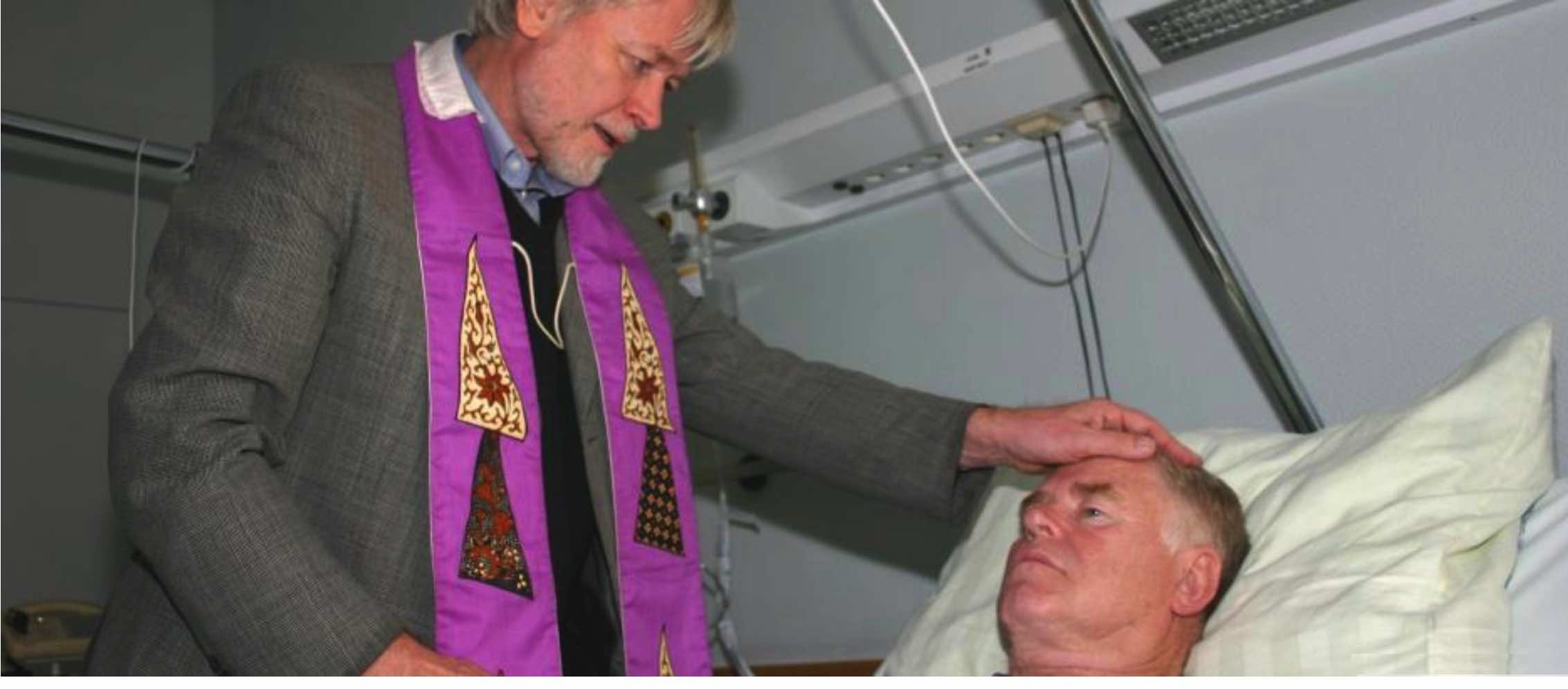 Priester segnet einem Mann in einem Krankenbett.