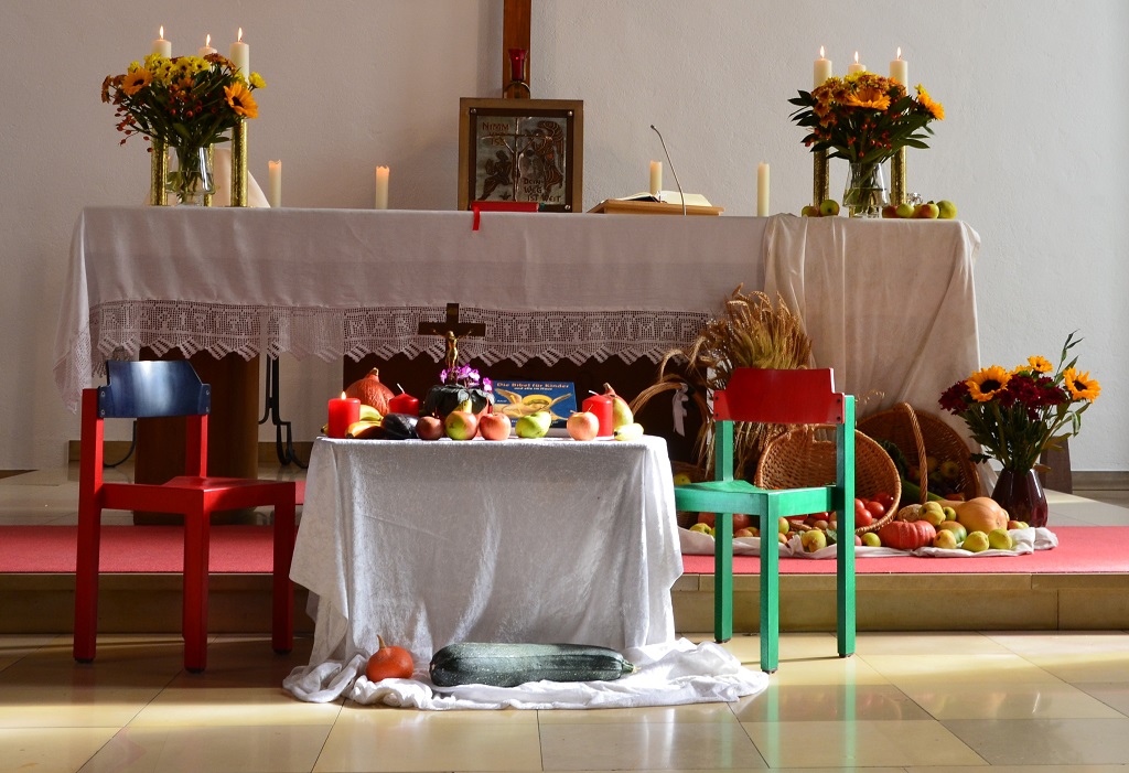 Ein kleiner Tisch mit Obst, Gemüse, Blumen, Kerzen, einer Bibel und einem Kreuz steht vor einem Altar.