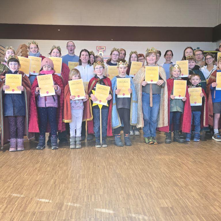 Eine Gruppe von Kindern, Jugendlichen und Erwachsenen, gekleidet als Sternsinger und mit Sternsinger-Urkunden