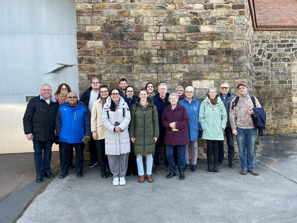 18 Männer und Frauen vor einer Mauer und einem großen Tor.