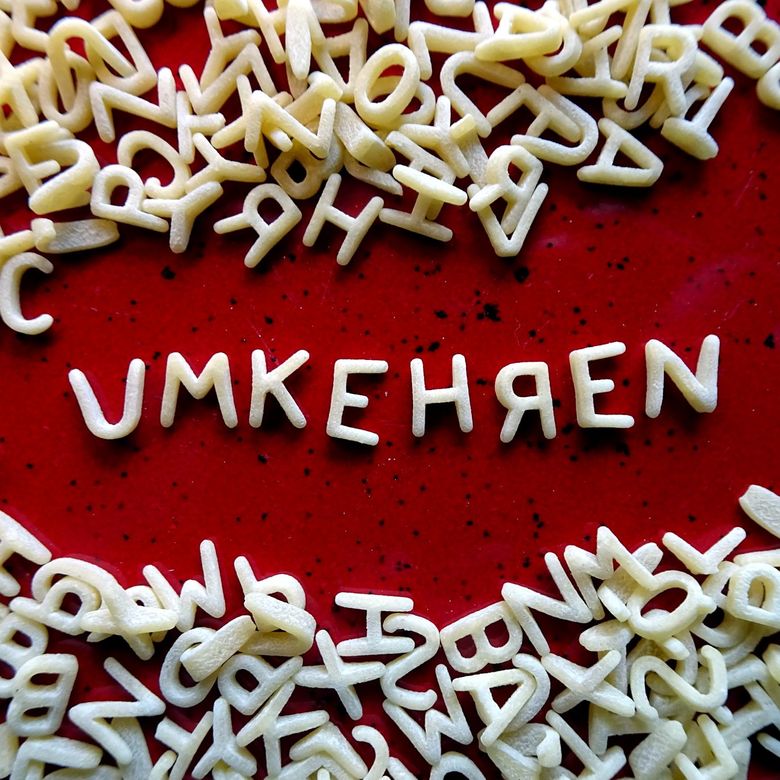 Buchstabennudeln auf rotem Hintergrund, in der Mitte das Wort „umkehren“, mit seitenverkehrt geschriebenem R.
