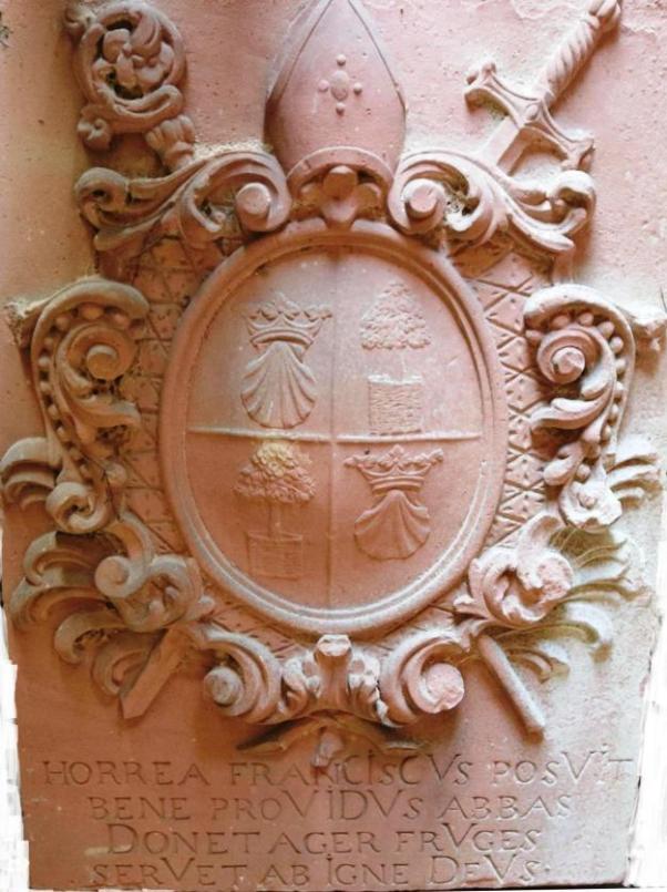 Wappen des Abtes Franziskus (1734-1756) an einer ehemaligen Klosterscheune in Planig. Das Sandsteinrelief ging 2018 verloren. Übersetzung der lateinischen Inschrift: 'Der fürsorgliche Abt Franziskus errichtete die Scheunen, schenke das Feld Früchte, bewahre sie Gott vor Feuer.'