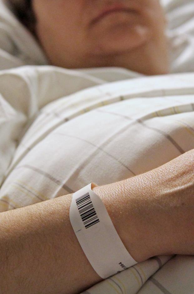 Person im Krankenhausbett mit Patientenarmband am Handgelenk.
