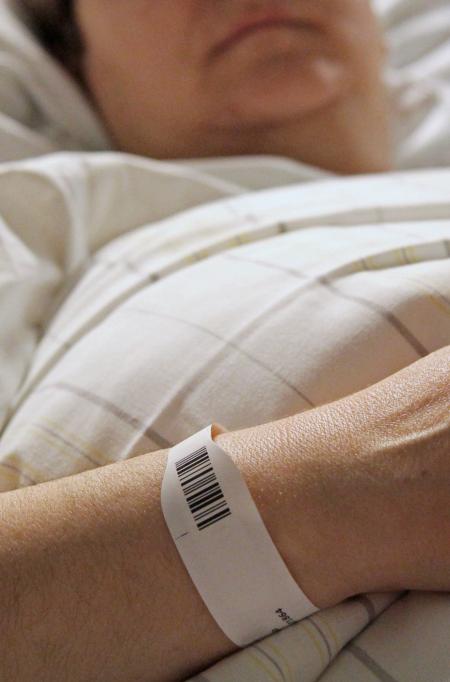 Person im Krankenhausbett mit Patientenarmband am Handgelenk.