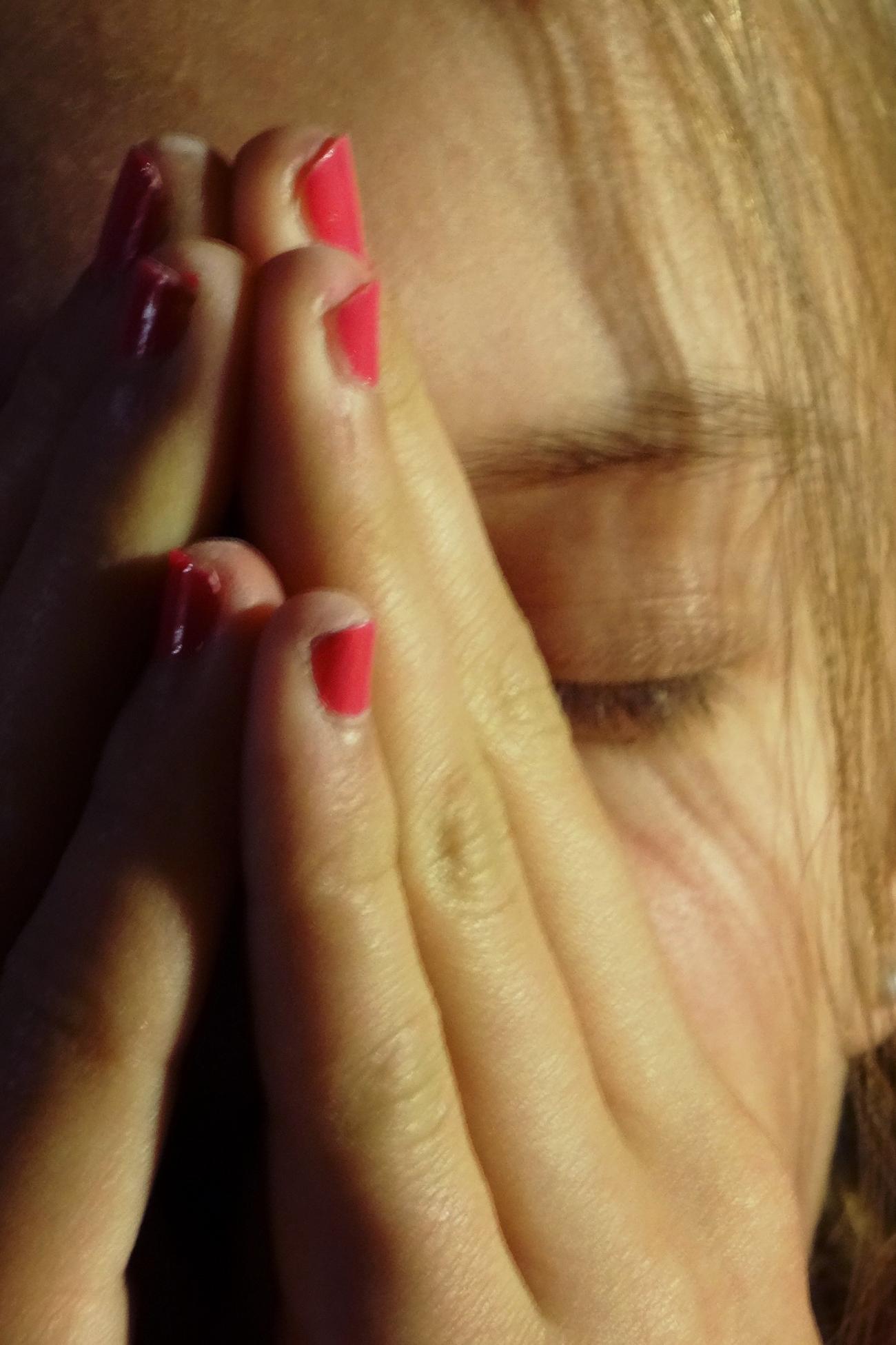 Frau hält Hände vors Gesicht, Augen geschlossen, pink lackierte Nägel