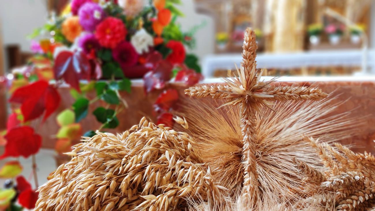 Nahaufnahme von kunstvoll gebundenen Getreideähren und einem Kreuz aus Getreideähren vor einem herbstlich geschmückten Altar