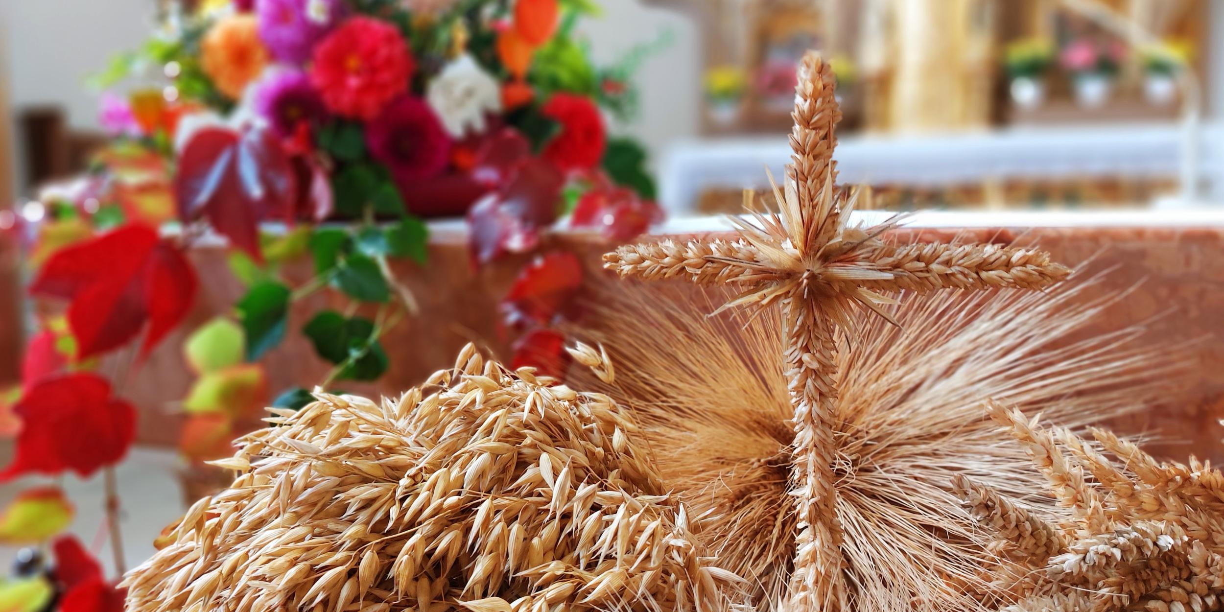 Nahaufnahme von kunstvoll gebundenen Getreideähren und einem Kreuz aus Getreideähren vor einem herbstlich geschmückten Altar