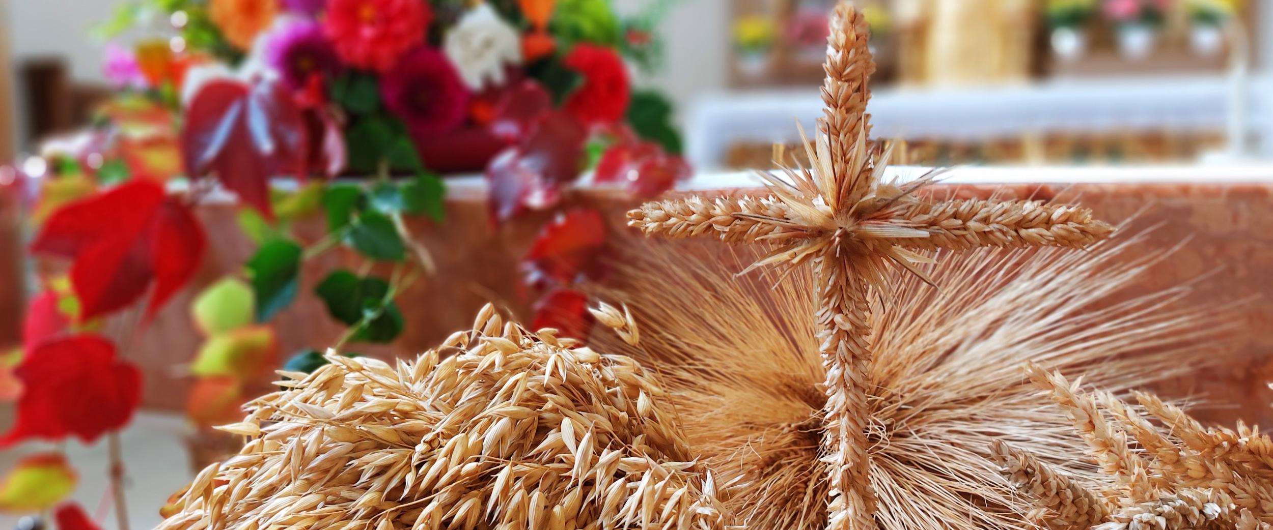 Nahaufnahme von kunstvoll gebundenen Getreideähren und einem Kreuz aus Getreideähren vor einem herbstlich geschmückten Altar