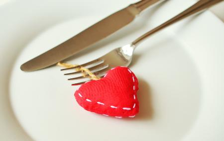 Rotes Stoffherz auf Teller, daneben Gabel und Messer.