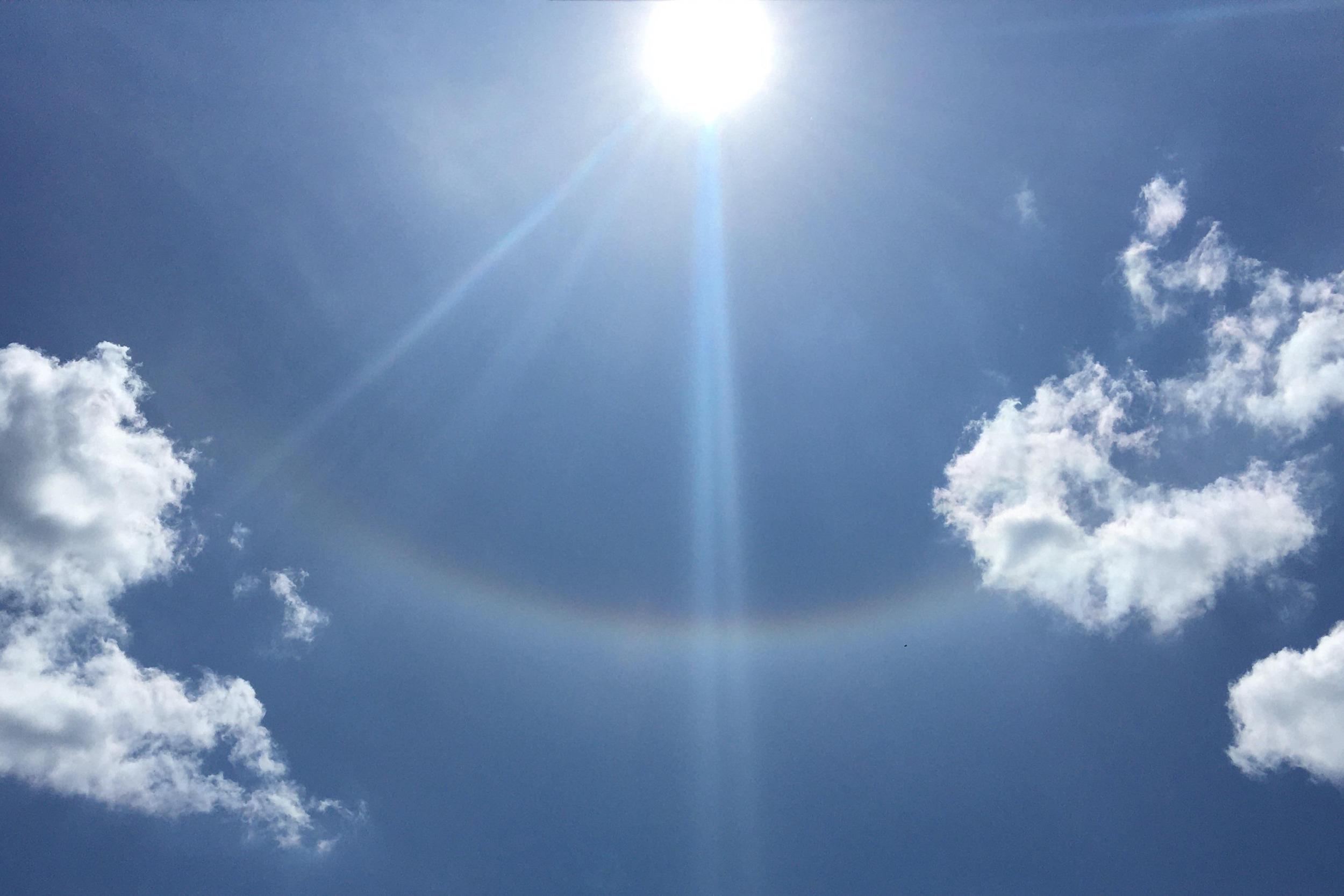 Sonne am blauen Himmel mit leichten Wolken und einem schwachen Lichtbogen