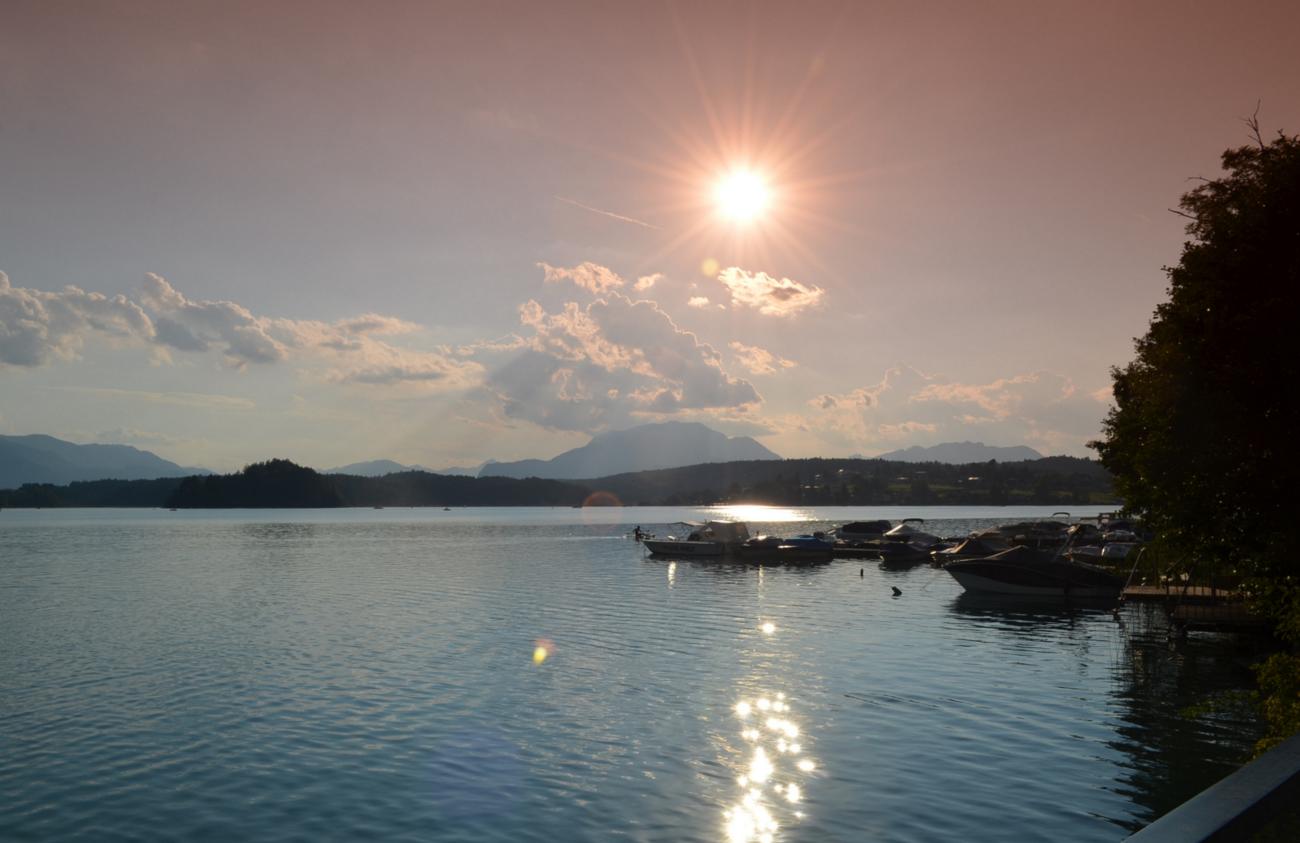 Sonnenuntergang am See mit Booten am Steg und Bergen im Hintergrund