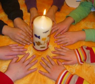 Kinderhände rund um eine brennende Kerze