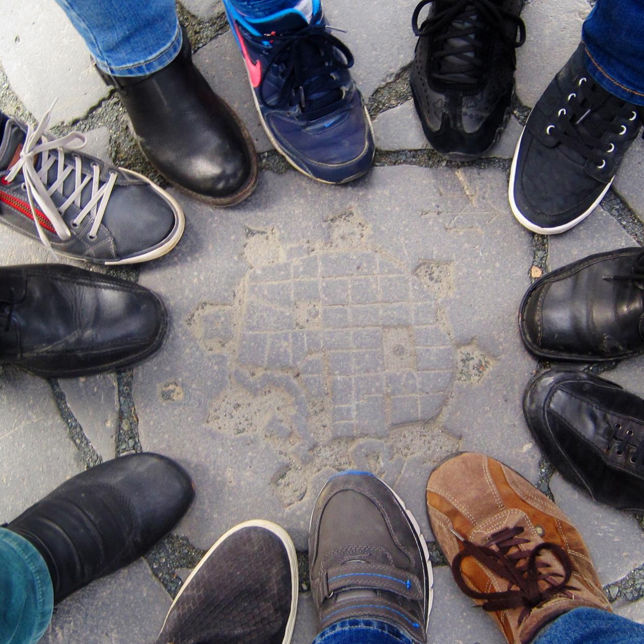 Mehrere Menschen stehen im Kreis, nur ihre Schuhe sind sichtbar.