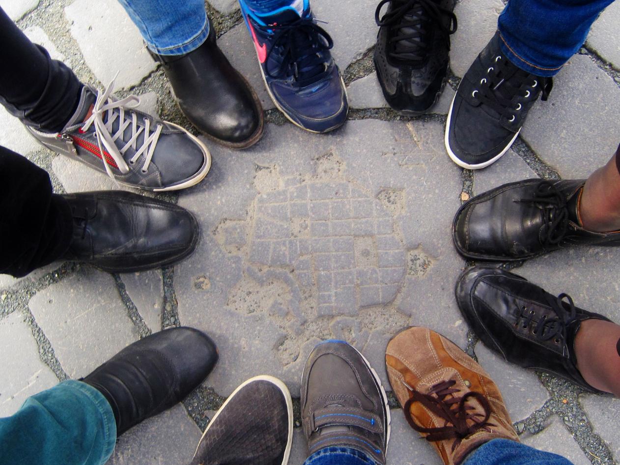 Mehrere Menschen stehen im Kreis, nur ihre Schuhe sind sichtbar.