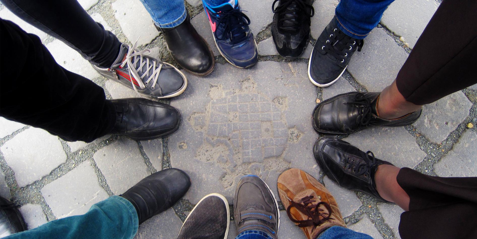 Hin zur Mitte Mehrere Menschen stehen im Kreis, nur ihre Schuhe sind sichtbar.