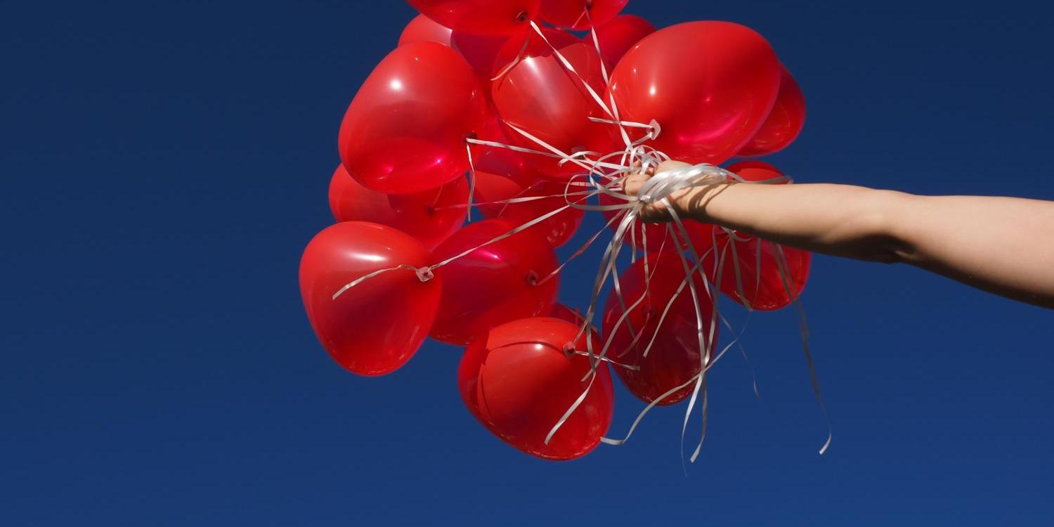 Hand hält rote Luftballons vor klarem, blauem Himmel