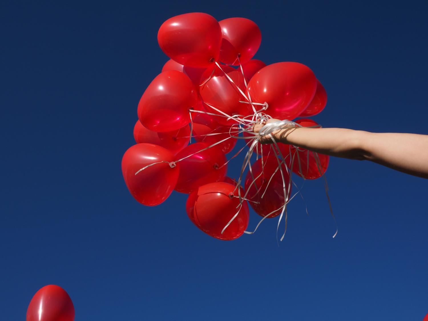 Hand hält rote Luftballons vor klarem, blauem Himmel