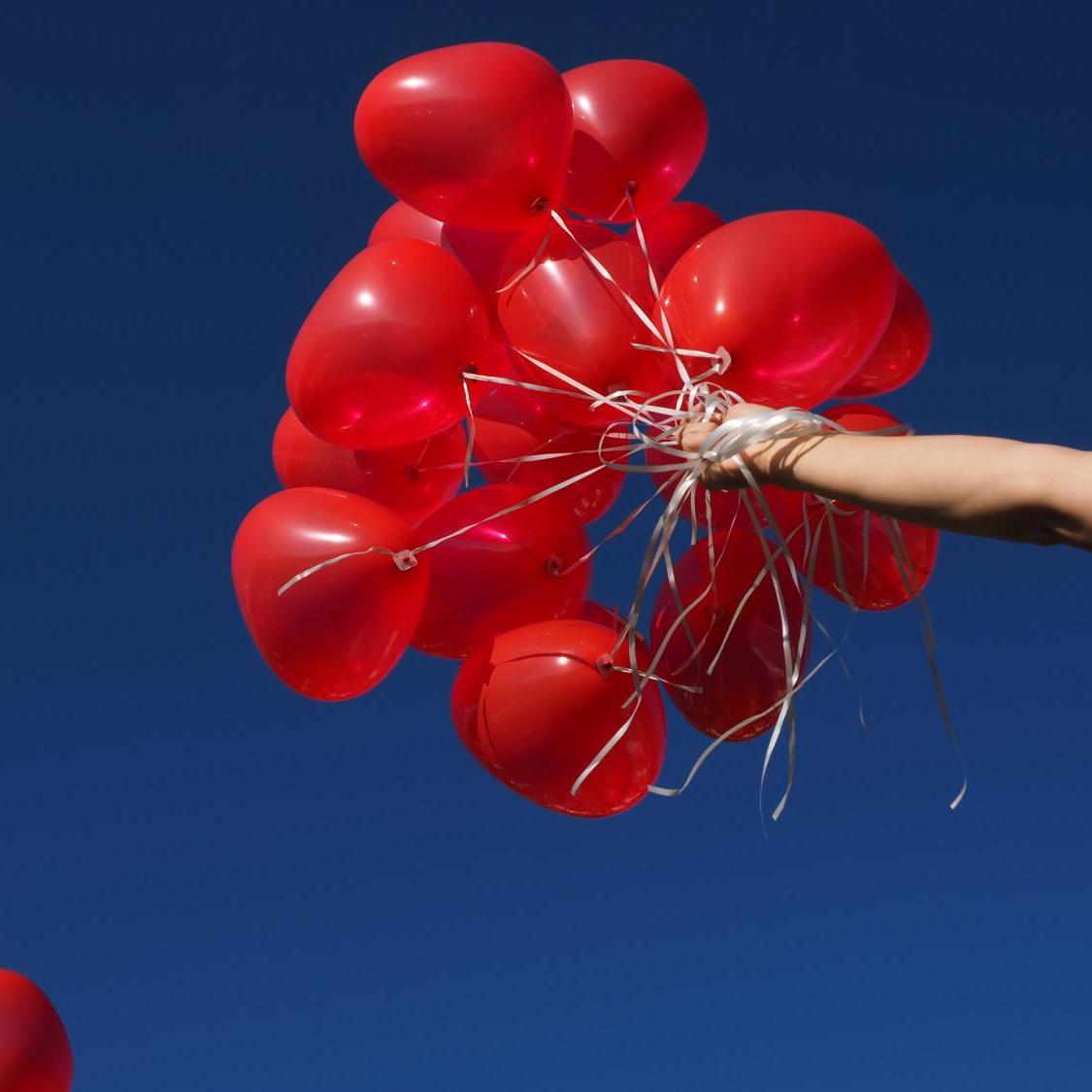 Hand hält rote Luftballons vor klarem, blauem Himmel
