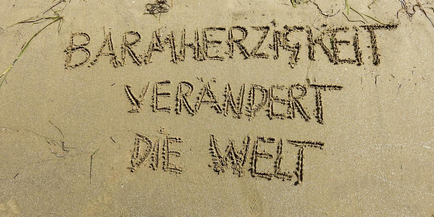 Text im Sand: 'Barmherzigkeit verändert die Welt'