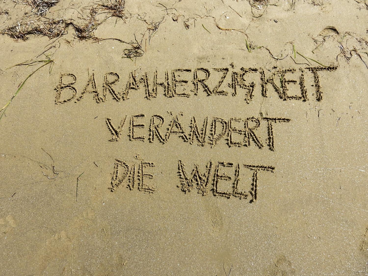 Text im Sand: 'Barmherzigkeit verändert die Welt'