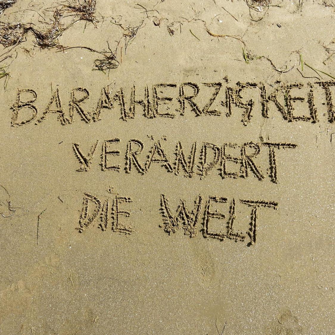 Text im Sand: 'Barmherzigkeit verändert die Welt'