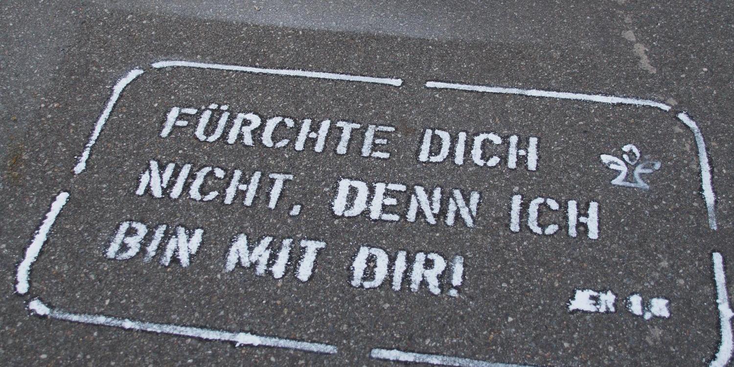 Beine einer Person auf Gehweg mit aufgemaltem ermutigendem Spruch in Weiß