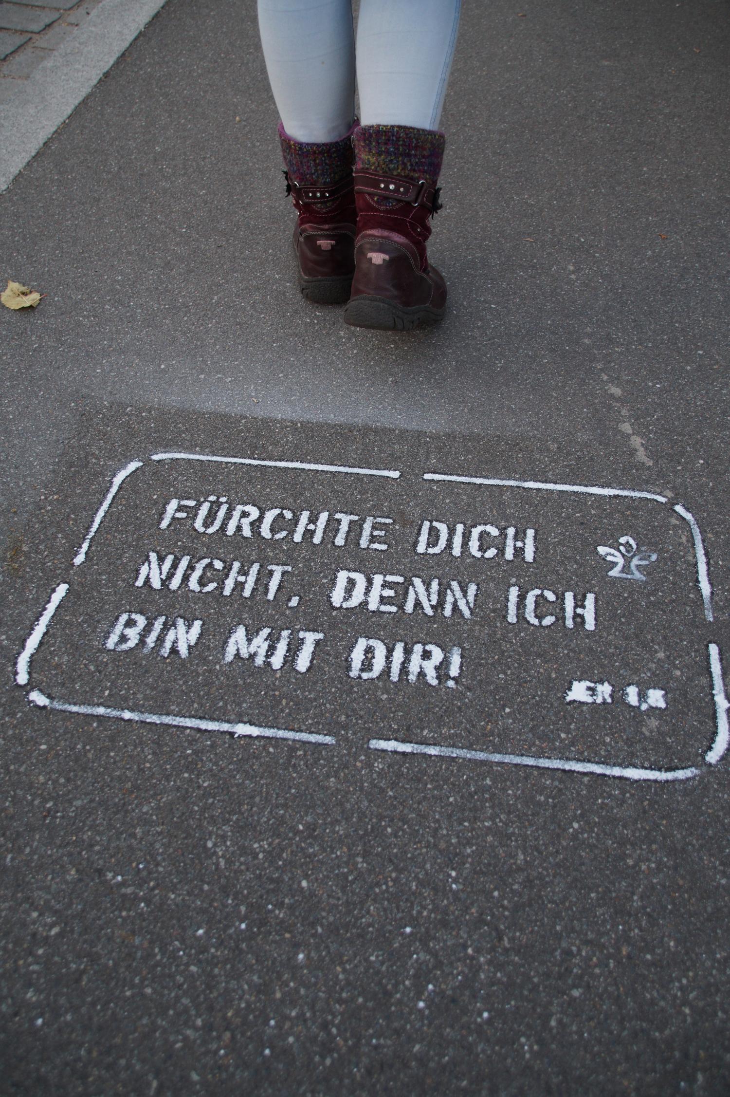 Beine einer Person auf Gehweg mit aufgemaltem ermutigendem Spruch in Weiß