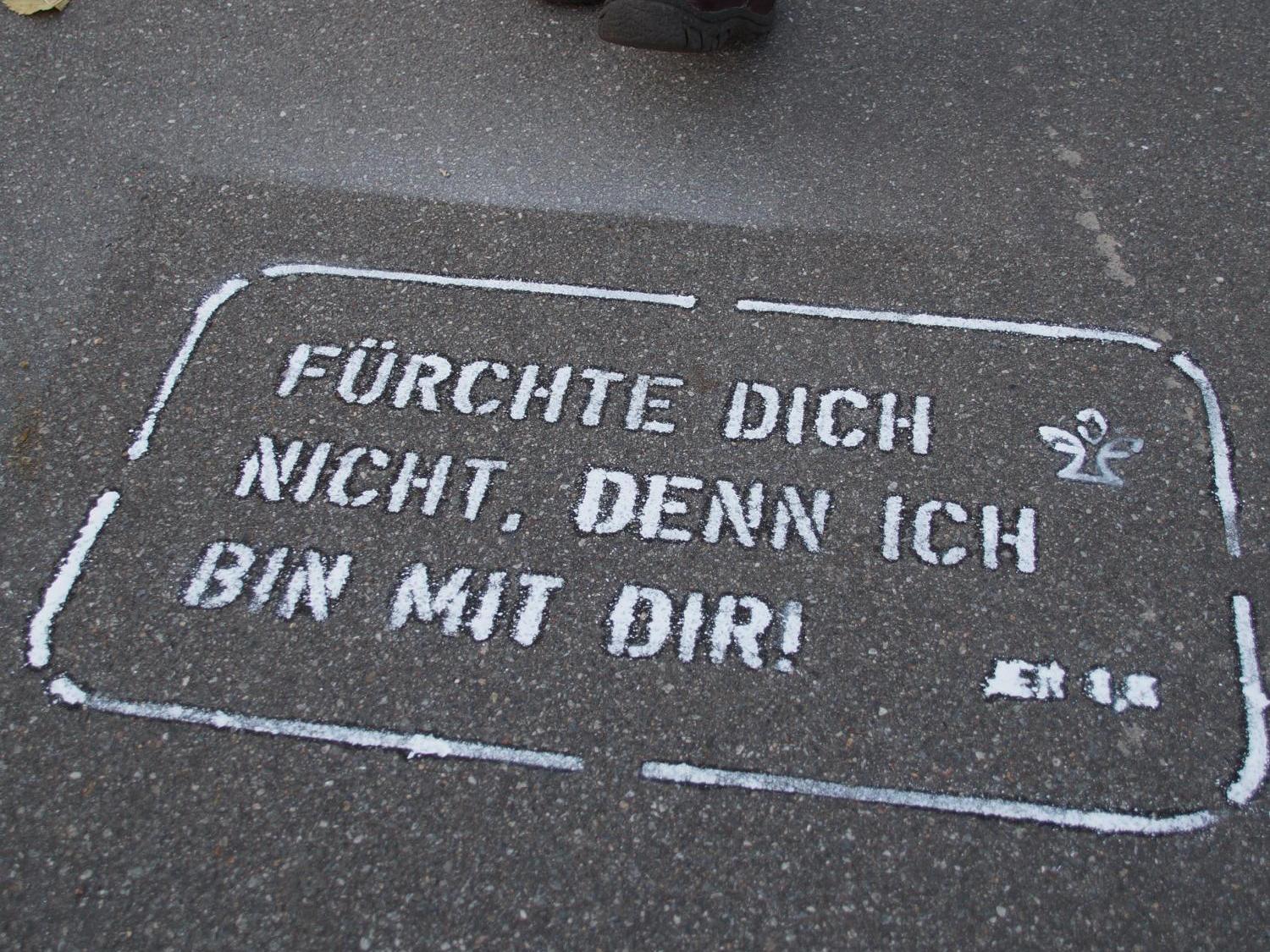 Beine einer Person auf Gehweg mit aufgemaltem ermutigendem Spruch in Weiß