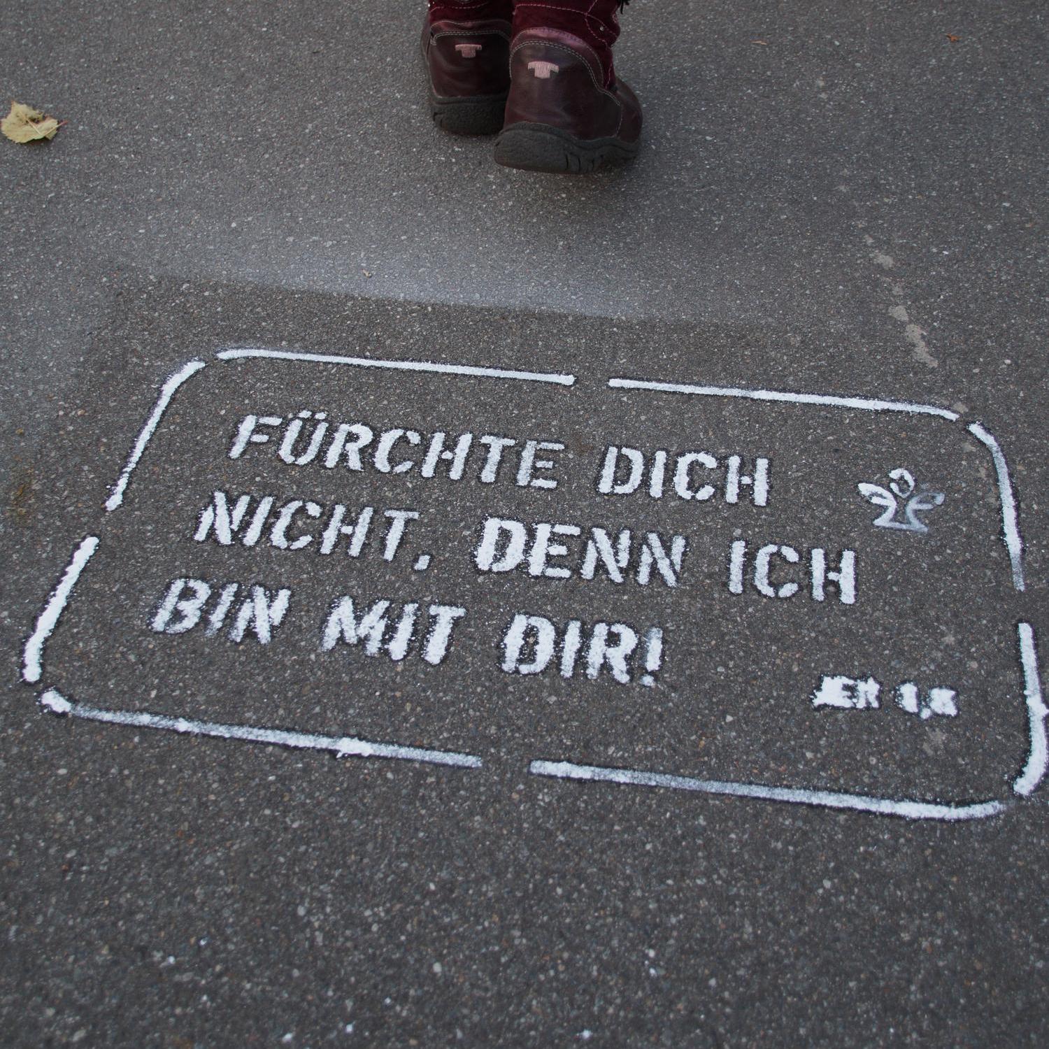 Beine einer Person auf Gehweg mit aufgemaltem ermutigendem Spruch in Weiß