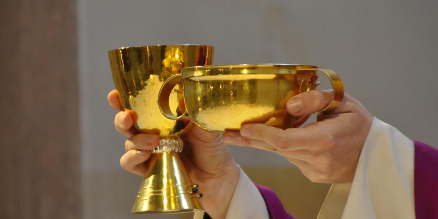Priesterhände halten Kelch und Hostienschale in die Höhe.