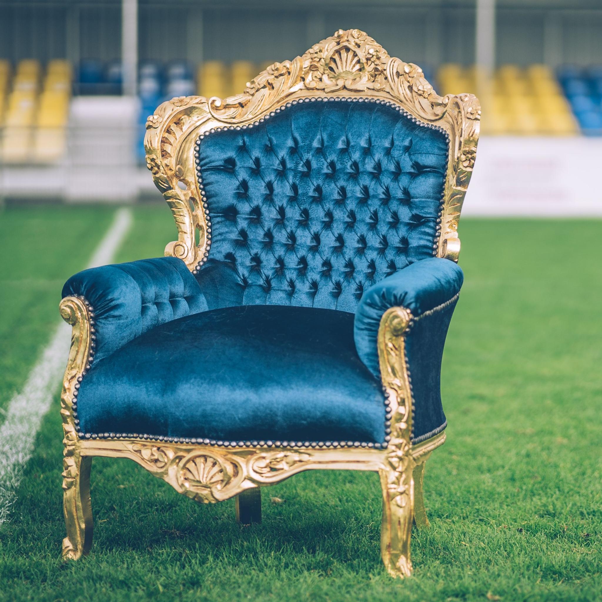 A luxurious blue velvet and gold armchair sits prominently on a sports field.