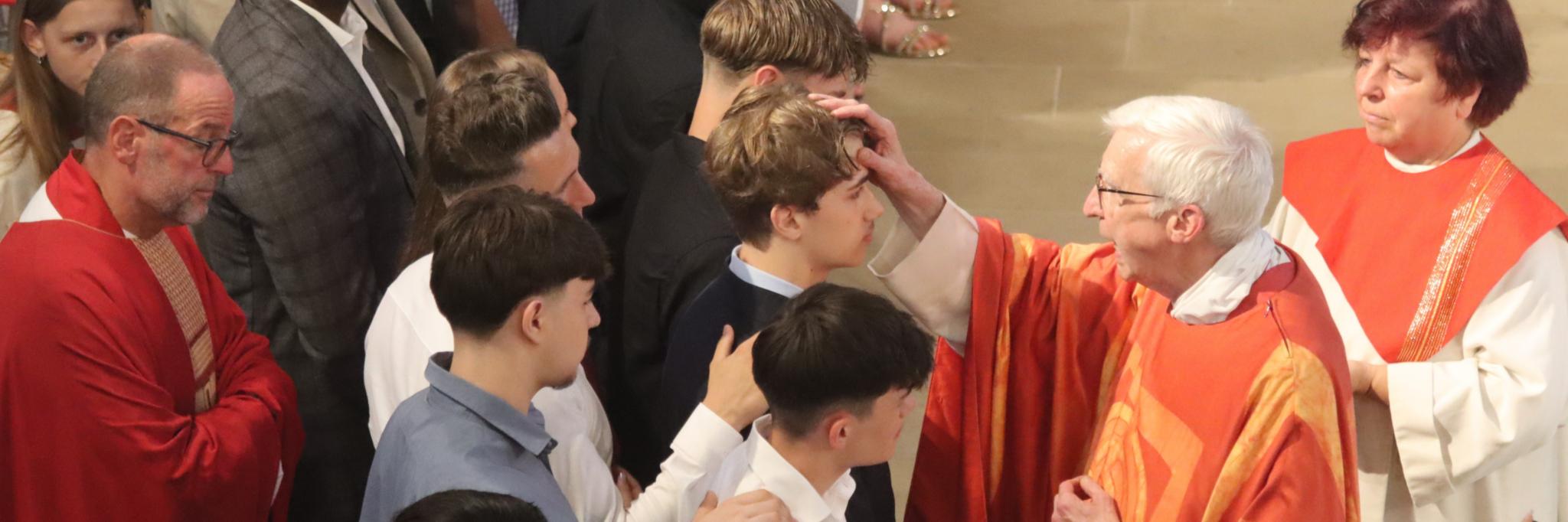 Domkapitular Weinert zeichnet ein Kreuz mit Chrisam auf die Stirn eines Jugendlichen