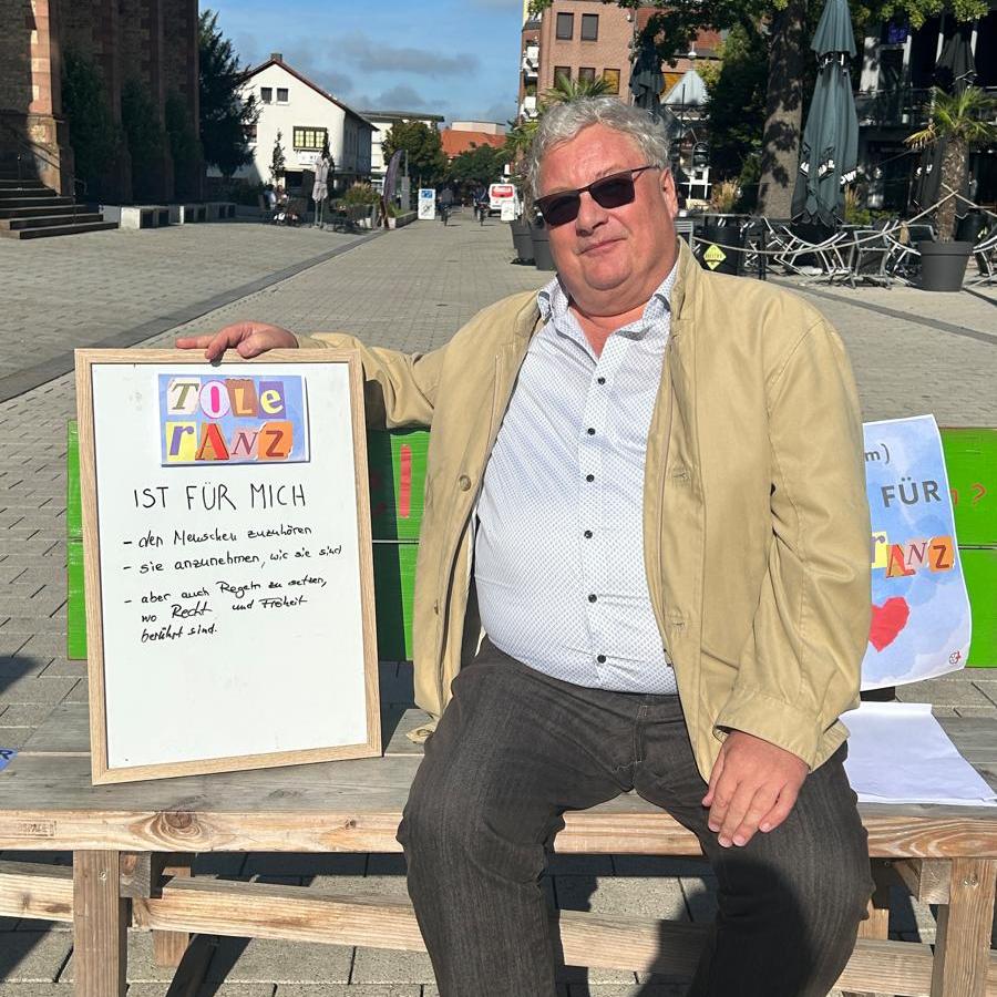 Mann auf einer Bank sitzend mit einem Schild 'Toleranz ist für mich'