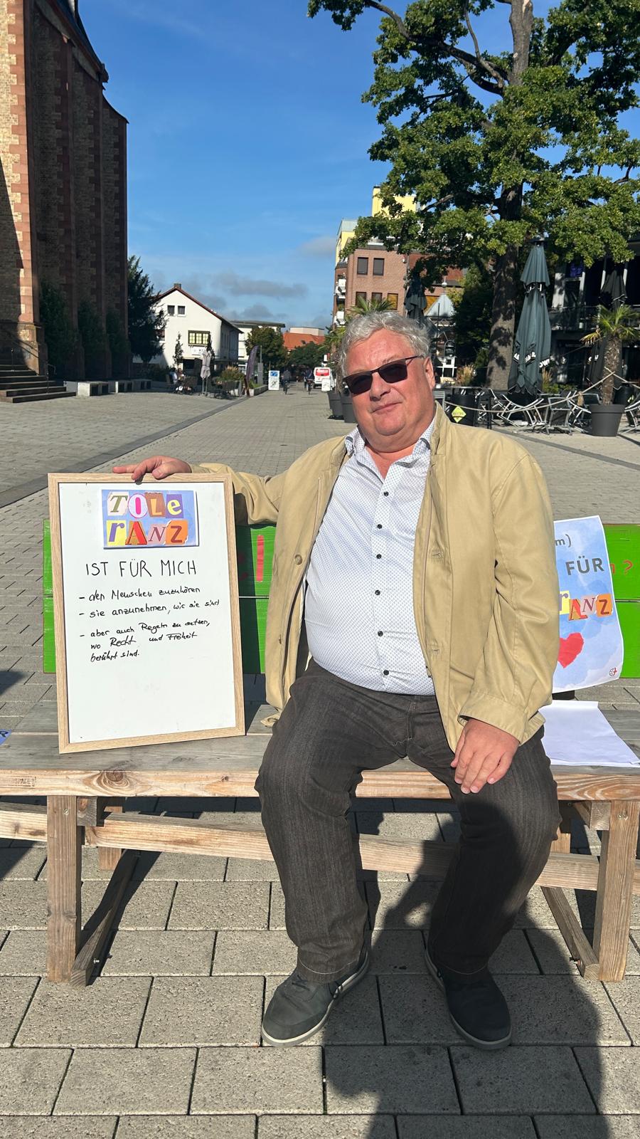Mann auf einer Bank sitzend mit einem Schild 'Toleranz ist für mich'