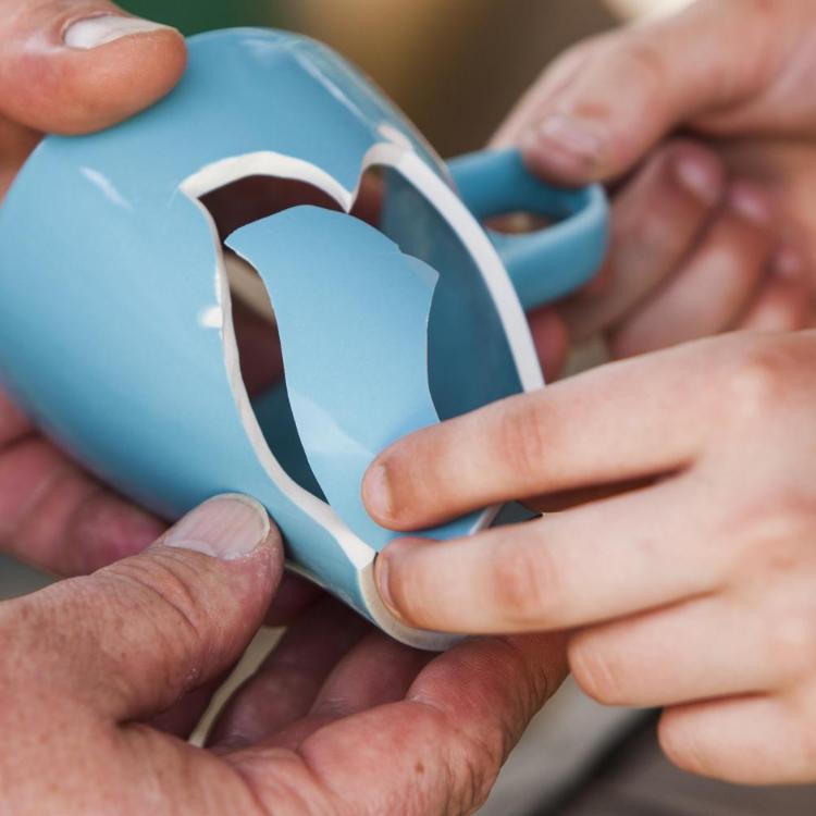 zwei Hände halten eine blaue Tasse, die zerbrochen ist