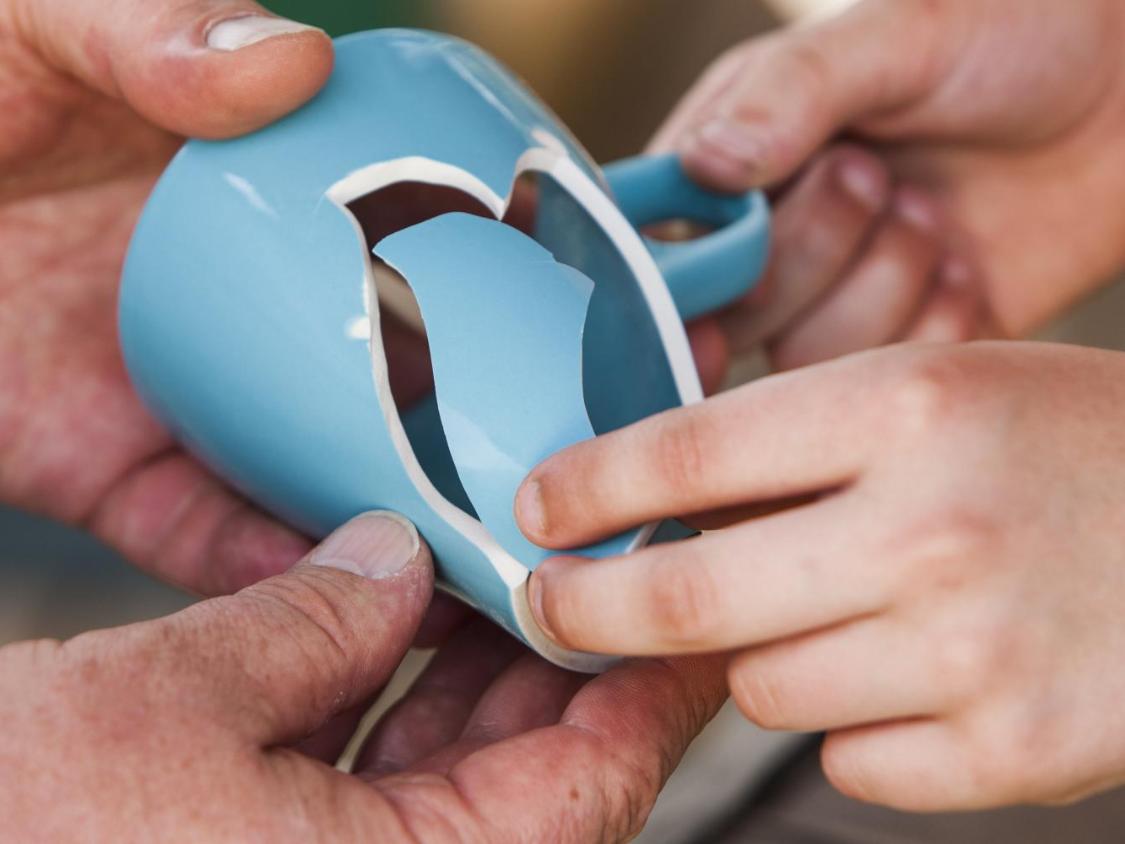 zwei Hände halten eine blaue Tasse, die zerbrochen ist