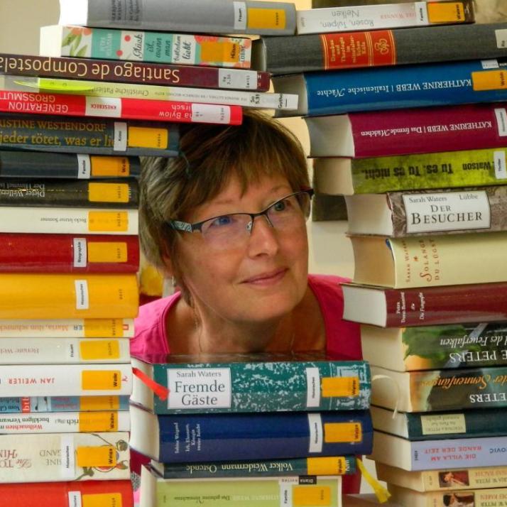 Frau schaut durch Bücherstapel (c) Borromäusverein e.V Frau schaut durch Bücherstapel