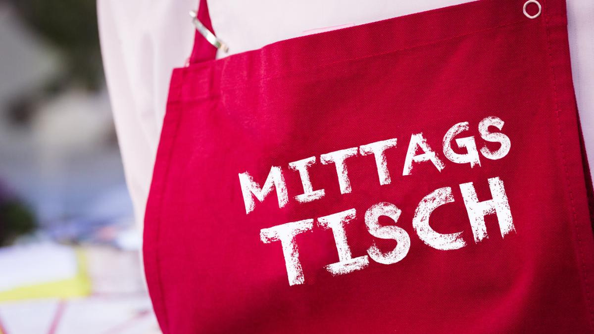 Person mit roter Kochschürze mit der Aufschrift 'Mittagstisch'